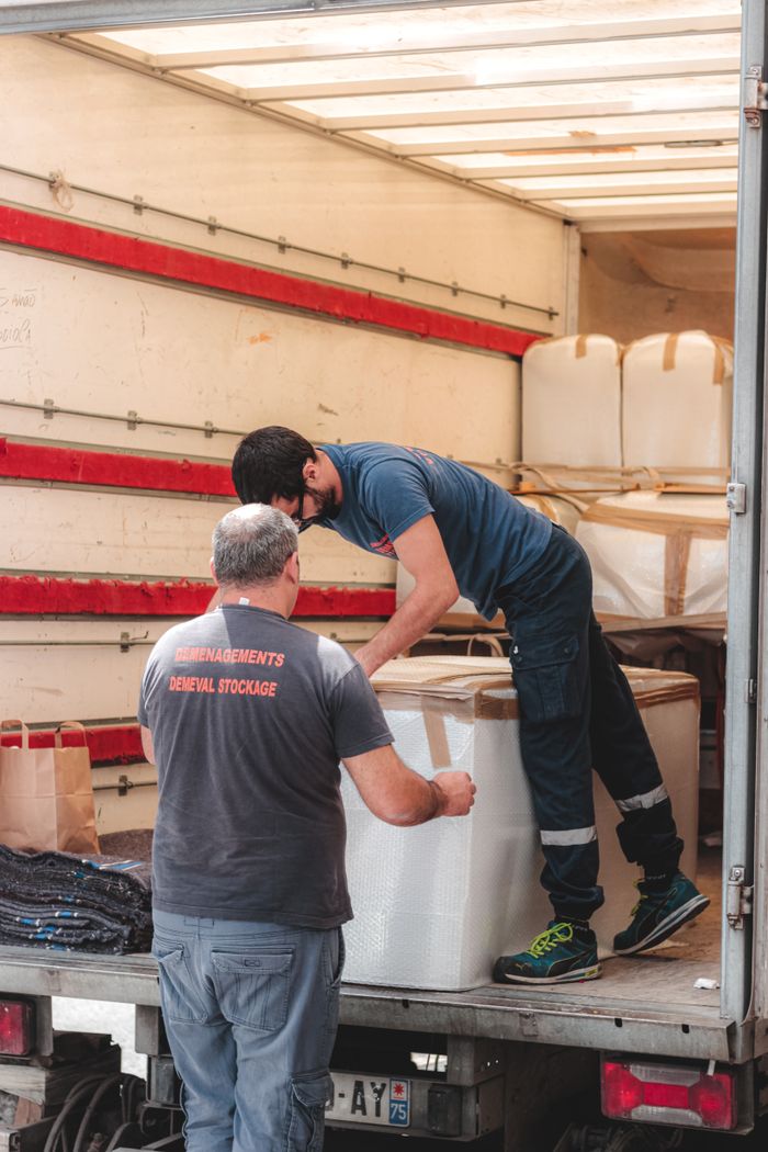 Faceless removal porters in uniform unloading big white boxes off lorry while working in  delivery service